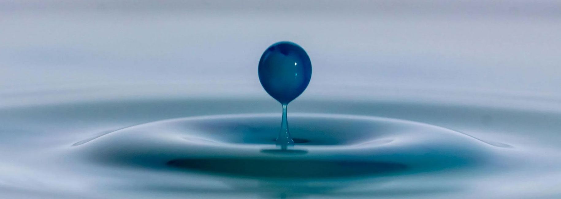 Blue water droplet creating ripples on surface.