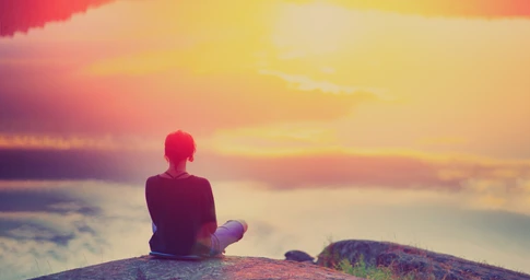 Person meditating by serene sunset lake