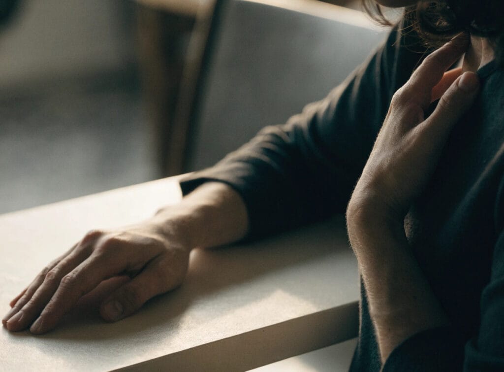 Person touching neck while sitting at table