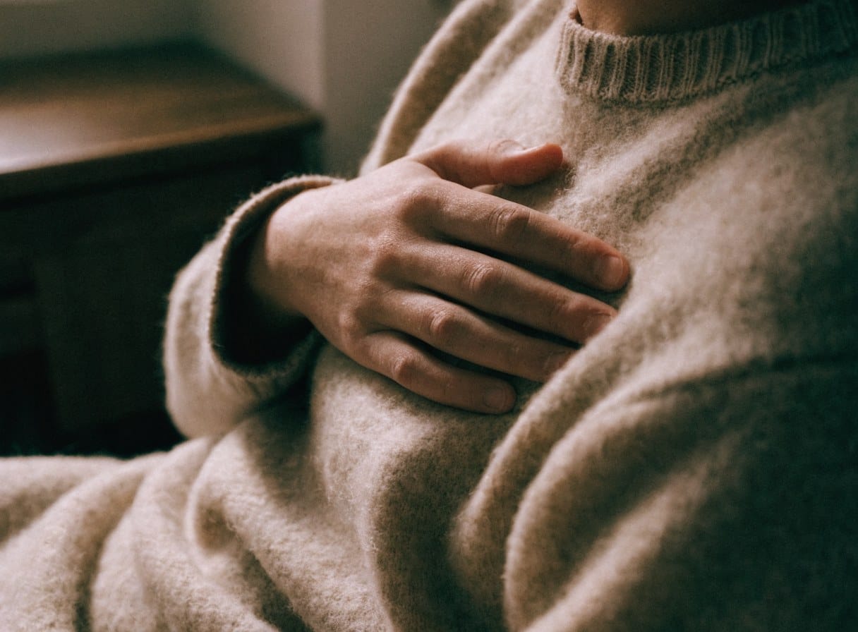 Close-up of a hand resting on the chest over a wool jumper in soft window light